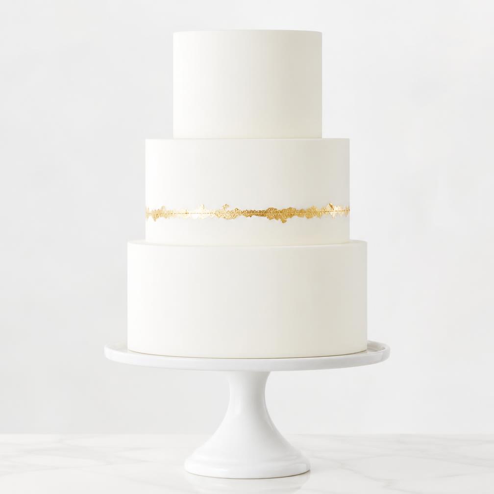 A clean minimal white tiered wedding cake with a smooth matte finish and a single thin ribbon of gold leaf detail